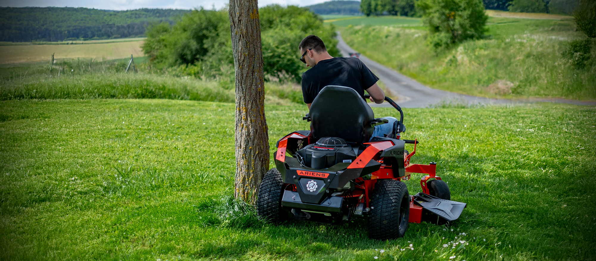 Mann mäht mit Ariens Zero-Turn-Aufsitzmäher nahe an einem Baum auf einer Wiese